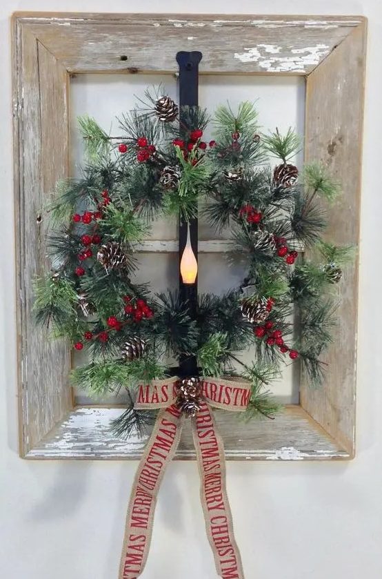 a window frame wreath of faux evergreens, berries and pinecones with a burlap bow and a light