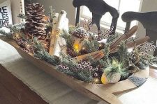 a wooden dough bowl with evergreens, berries, branches, pinecones, lights and small skis