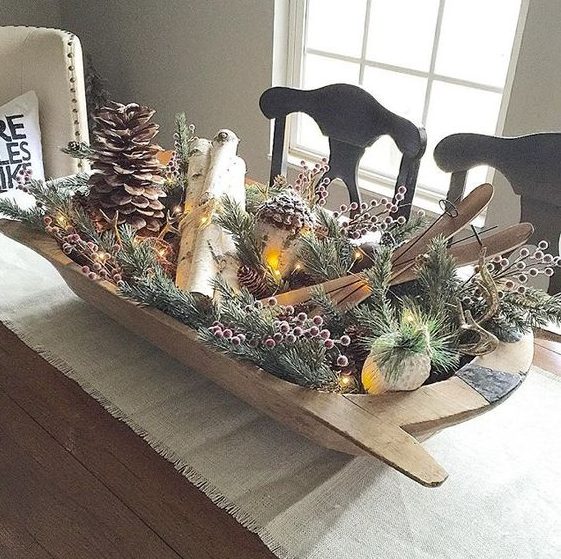 a wooden dough bowl with evergreens, berries, branches, pinecones, lights and small skis