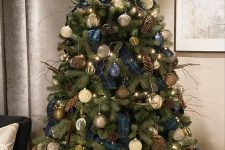 a woodland Christmas tree decorated with pinecones, branches, feathers, navy plaid ribbons, white and silver and brown ornaments