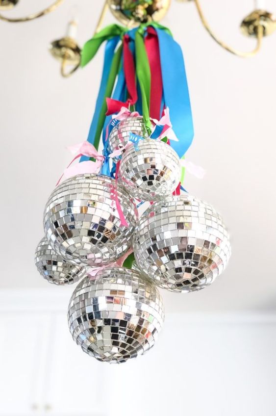 disco balls hanging on bright ribbons are amazing to style your space for NYE, hang them on a chandelier