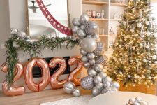 fun NYE party decor with balloon numbers, evergreens, disco balls and a garland of silver balloons