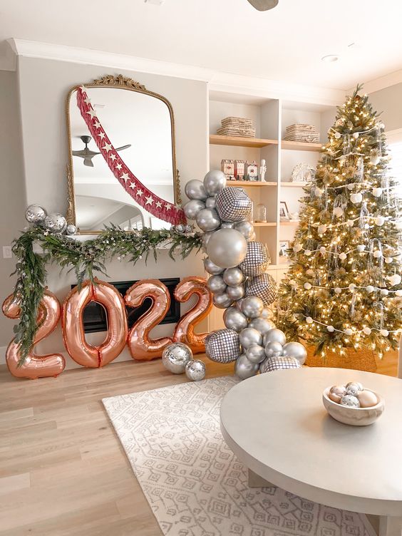 fun NYE party decor with balloon numbers, evergreens, disco balls and a garland of silver balloons