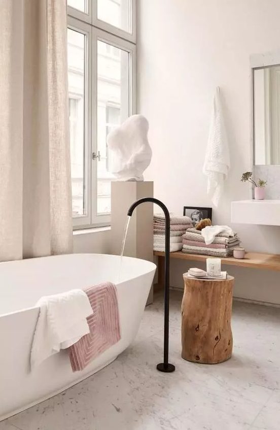 A lovely spa bathroom with an oval tub and a black faucet, a floating shelf, a wall mounted sink and a sculpture on a stand