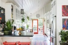 06 a catchy eclectic kitchen with white cabinets, bold red stools and doors, pendant lamps and potted greenery