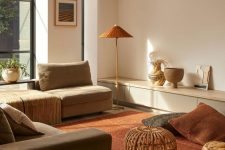 08 a contemporary warm earthy living room with a grey sofa and neutral seats, a deep red carpet and pillows, a floor lamp and an amber pouf