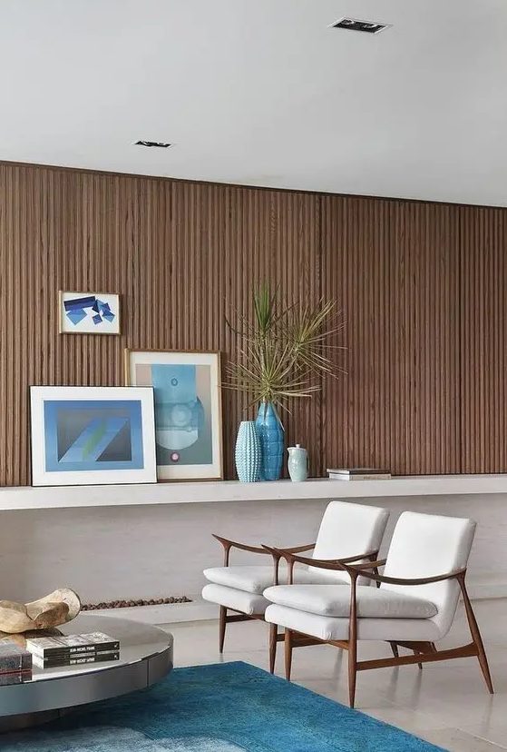 a beautiful ocean-inspired living room with a wood slat accent wall, neutral chairs, a low coffee table, some blue decor and textiles