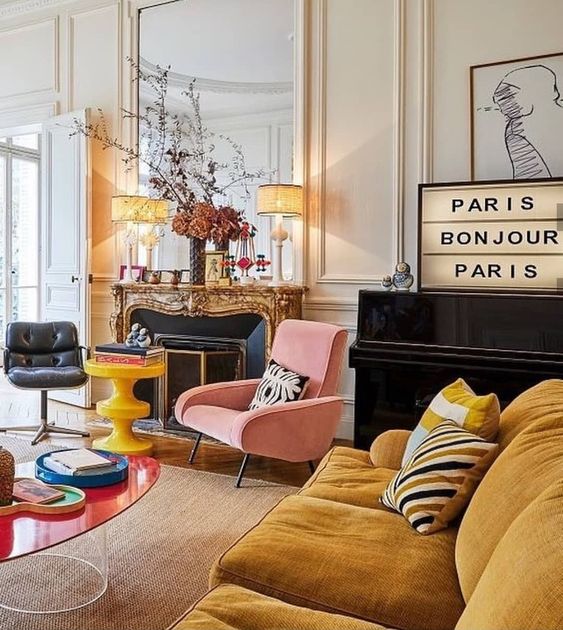 a pretty maximalist living room with a refined vintage fireplace, a mustard sofa, a pink and black chair, a red coffee table and lamps