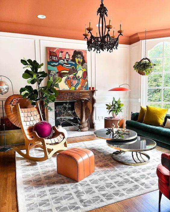 a bold living room with an orange ceiling, a rocker chair, a dark green sofa and colorful pillows, a fireplace, an orange pouf