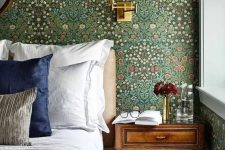 14 a classic English bedroom with vintage floral wallpaper, an upholstered bed with neutral bedding, a stained nightstand and a sconce