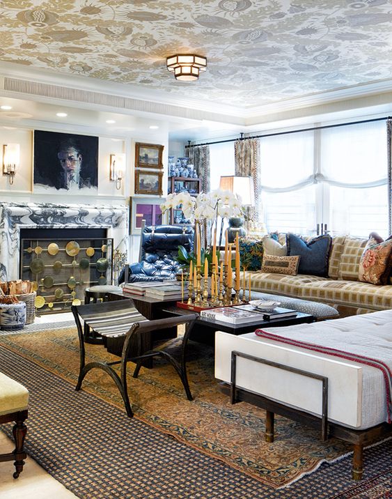 a maximalist living room with a marble fireplace, a printed sofa and a neutral daybed, layered rugs, colorful pillows