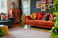 a colorful maximalist living room with a hunter green accent wall, a rust sofa and a colorful gallery wall, a printed rug, a dark green chair and an orange storage unit