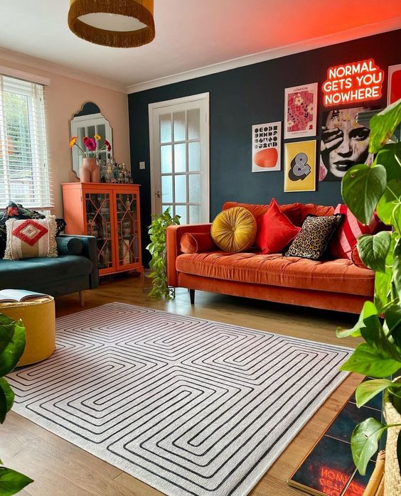 a colorful maximalist living room with a hunter green accent wall, a rust sofa and a colorful gallery wall, a printed rug, a dark green chair and an orange storage unit
