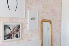 16 a pink bedroom with floral wallpaper, a white bed and pink and white bedding, some art and a mirror in a gold frame