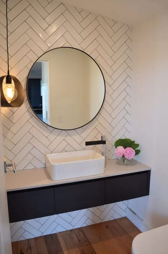 a sink zone with white herringbone tile, a built-in vanity, a round mirror and a pendant lamp is a cool and minimal space