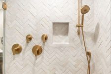 18 a neutral shower space completely clad with herringbone tiles, with a niche and some brass accents