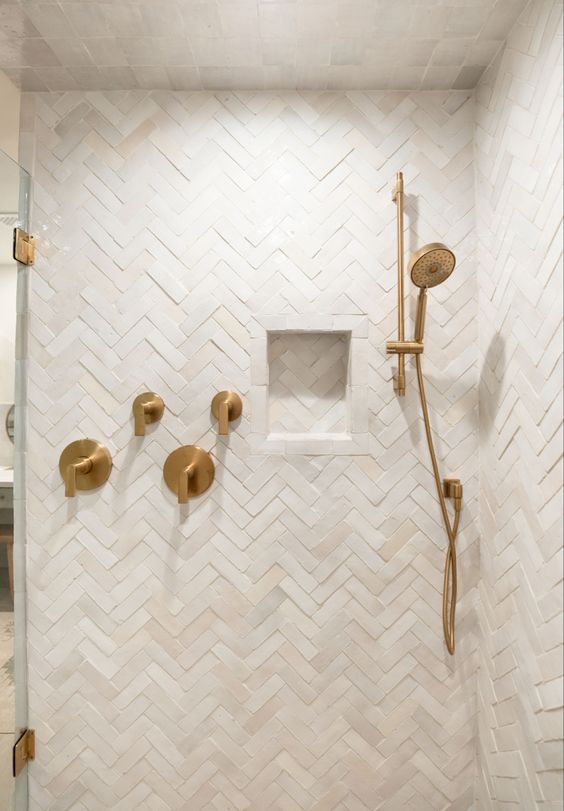 a neutral shower space completely clad with herringbone tiles, with a niche and some brass accents