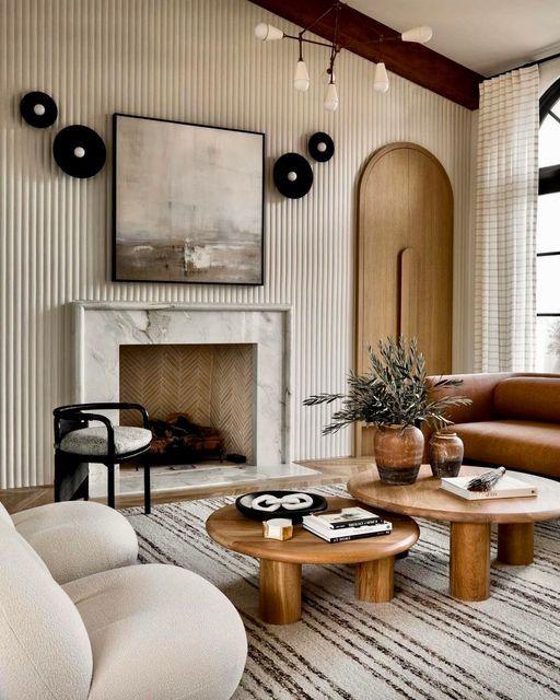 a beautiful and refined neutral living room with a fluted wall, a marble fireplace, wooden coffee tables, a leather sofa and neutral chairs