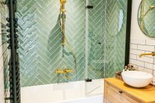 19 a cozy bathroom with green herringbone and white skinny tiles, a stained vanity, an oval tub and gold touches