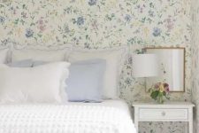 19 an English cottage bedroom with lovely pastel floral wallpaper, a bed with white and pastel blue bedding, a white nightstand and a mirror