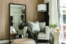 20 a lovely boho space with a wood slat accent wall, a neutral chair, a floor lamp, a mirror, layered rugs and jute poufs