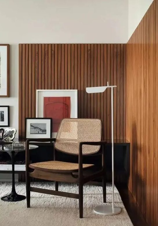 A mid century modern living room with stained wood slat accent walls, a rattan chair, a black table and bright artwork