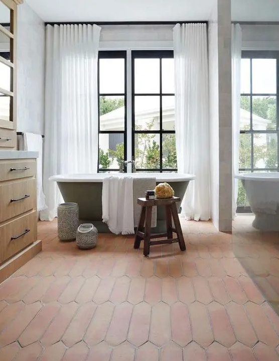 A farmhouse bathroom with a glazed wall, a green bathtub, a stained vanity, a terracotta tile floor and a glass enclosed shower