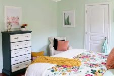 22 a mint-colored bedroom with a bed and floral bedding, a black and white dresser, a neutral chair and a chandelier