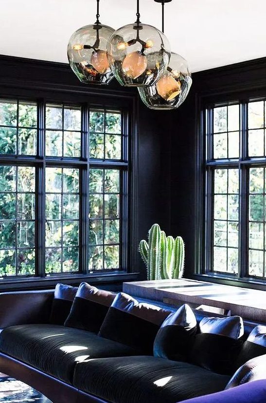 a moody living room in black, with a black and violet sofa, a console table, glass bubble lamps