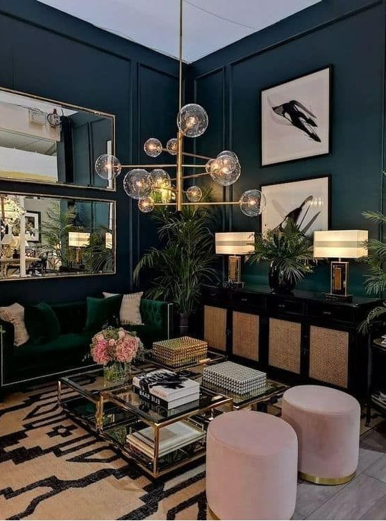 a chic moody living room with navy walls, a green sofa, a black credenza, pink poufs and a glass coffee table