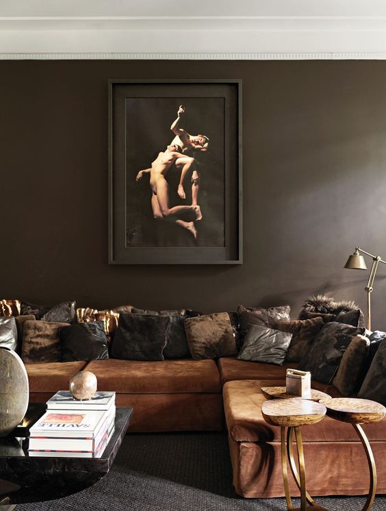 a moody living room with soot walls, a rust-colored sectional, lots of dark pillows, a coffee table with books