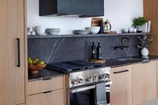 31 a light-stained kitchen with flat panel cabinets, black soapstone countertops and a backsplash, a black hood and black hardware