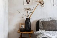 33 a catchy bedroom with light grey limewashed walls, a black bed with grey bedding, a wooden nightstand with dried blooms