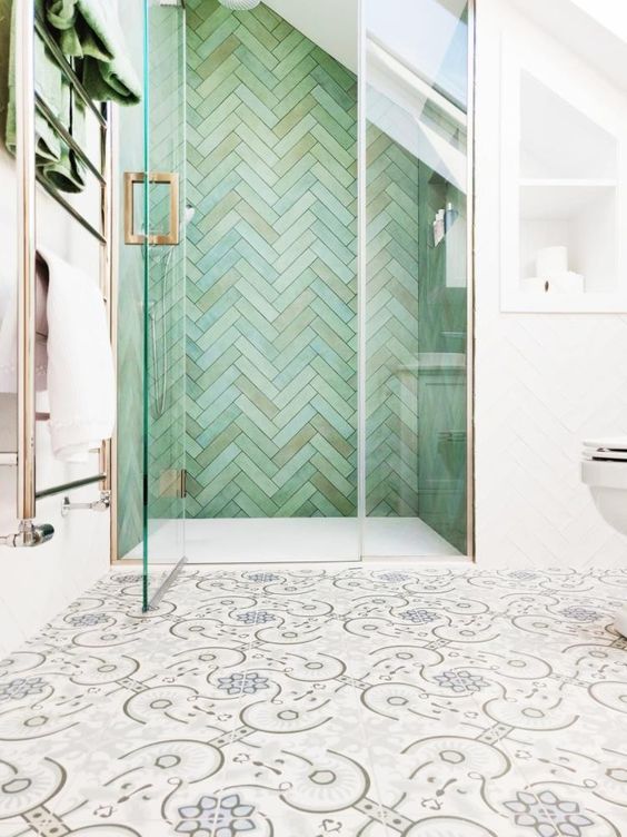 a creative bathroom with patterned tiles on the floor and an attic shower space clad with green herringbone tiles
