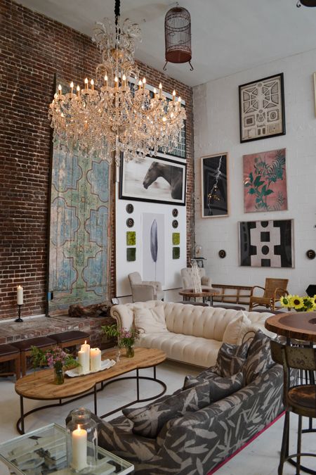 an eclectic living room with a brick accent wall, a neutral and printed sofa, a large gallery wall and a crystal chandelier