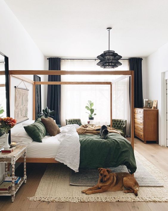 An eye catchy bedroom with a stained canopy bed, green chairs, a stained dresser, nightstands, artwork and a black pendant lamp