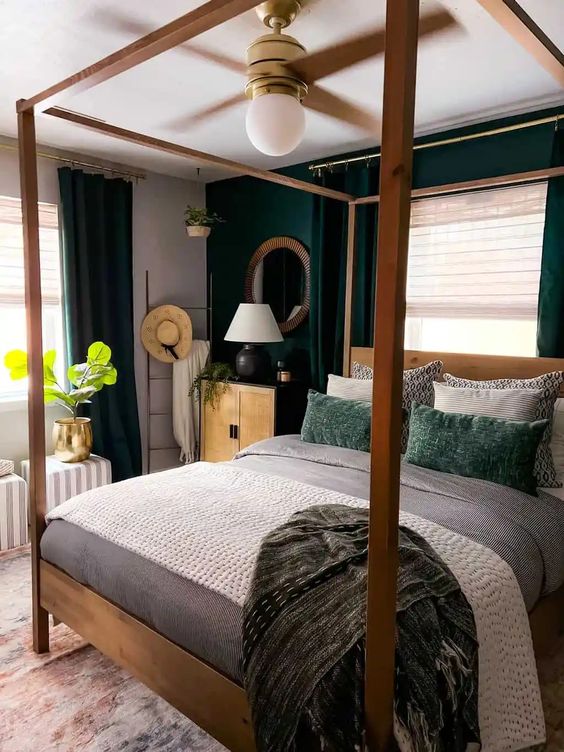 a small bold bedroom with a dark green accent wall and ceurtains, a canopy bed and neutral and green bedding and stripes poufs