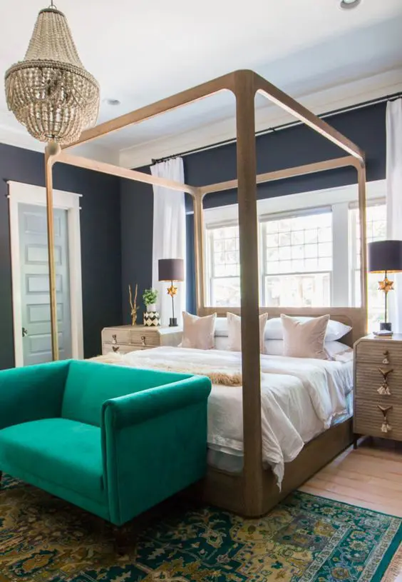 a moody bedroom with soot walls, a canopy bed and wooden nightstands, an emerald sofa, a beaded chandelier