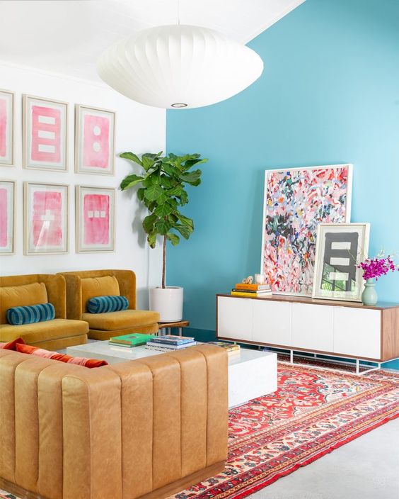 a dopamine decor living room with a blue accent wall, mustard chairs, an amber sofa, a low coffee table and some bold art