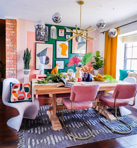 A dopamine infused dining room with a green accent wall, a gallery wall, a stained table, pink chairs and some white ones, bold decor