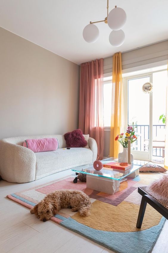 A dopamine infused living room with a creamy sofa, a colorful rug and bold curtains, bright pillows and some blooms