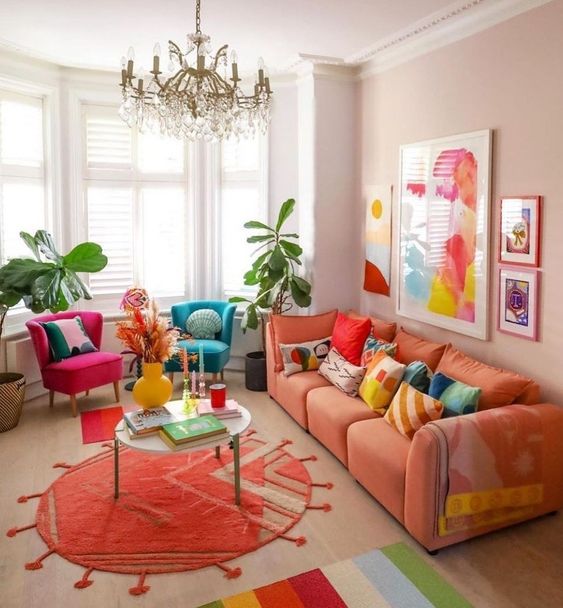 A bright dopamine infused living room with blush walls, an orange sofa, fuchsia and teal chair, bold artwork