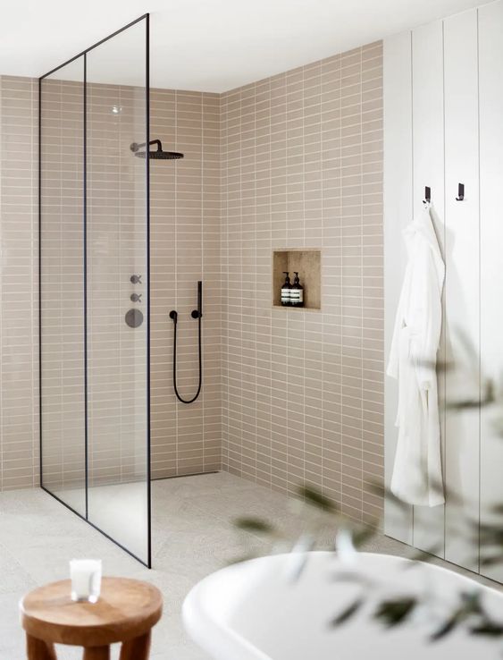 a neutral bathroom with planked walls and tan stacked tiles, a large shower space, black details for a contrast