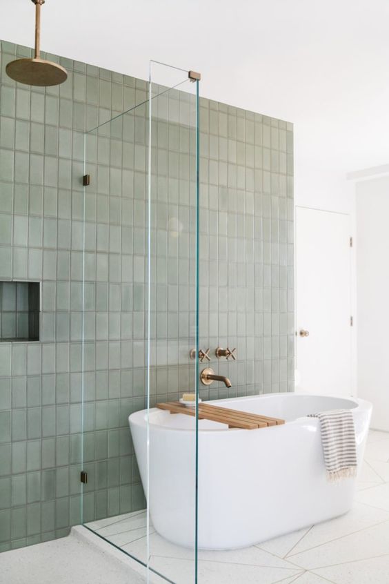 a modern bathroom with a geo floor, a green stacked tile wall, an oval tub and brass fixtures