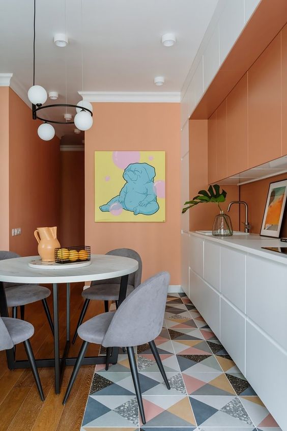 a Peach Fuzz kitchen with orange and white cabinets, a mirror backsplash, a white table and grey chairs is amazing