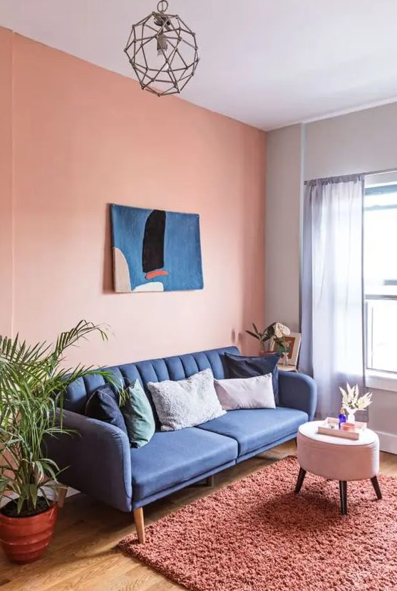 a Peach Fuzz living room with a cobalt blue sofa, a pouf, a coral rug, a blue artwork and potted plants