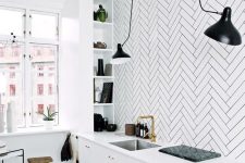 a Scandinavian kitchen with sleek white lower cabinets, a white herringbone tile backsplash, shelves, black lamps and a wooden stool