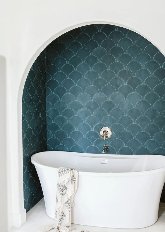 a bathing space in a niche, with navy scallop tiles, a chic tub and neutral fixtures is a cool space for soaking