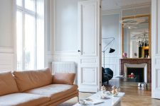 a beautiful Parisian chic living room with grey walls and herringbone floors, a peachy sofa and ottoman, a marble table, a fireplace and a black chair