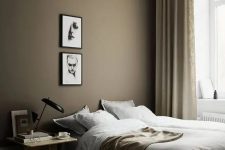 a beautiful Scandi bedroom with a taupe accent wall, a bed, a light-stained nightstand, a mini gallery wall and tan and gold touches